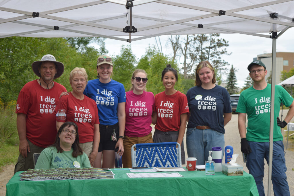 Eight volunteers at an educational booth, all wearing T-shirts saying, "I dig trees."