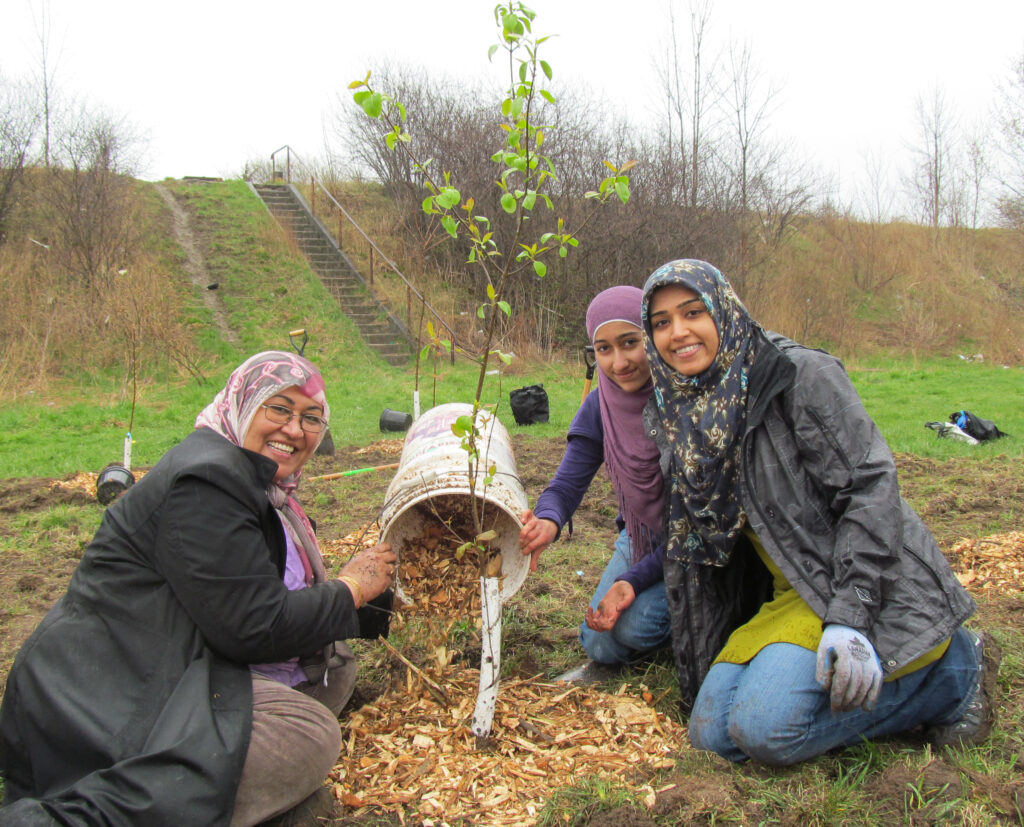 Three women with head scarves planting a tree. (Photo credit: ReForest London)