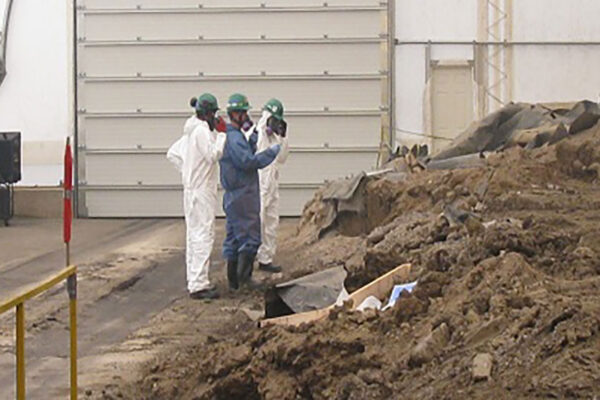 Three workers in hazmat suits at a toxic waste containment site.
