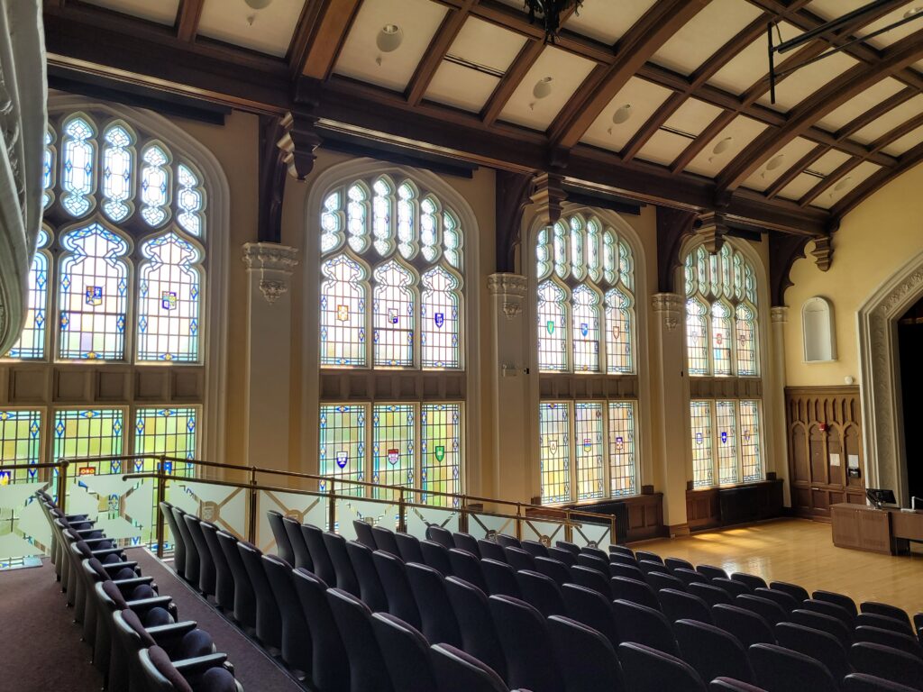 Inside view of Conron Hall, showing the auditorium and the wall of stained glass windows.