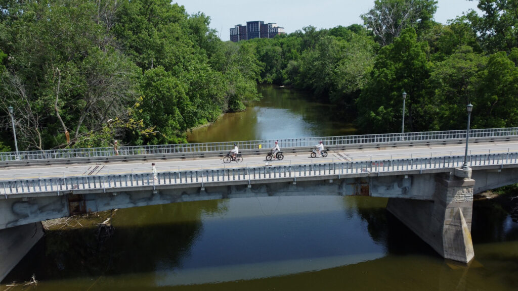 Three people on bicycles cross the historic University Drive stone bridge in London, Ontario.