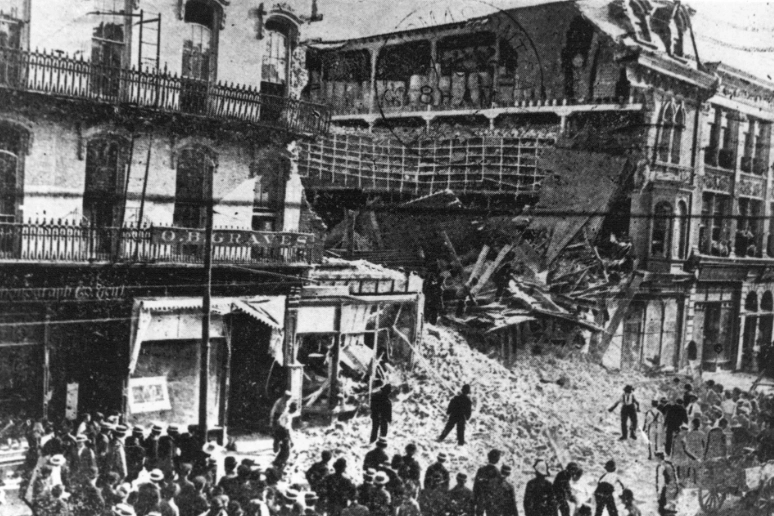 Reid's Crystal Hall Collapse, showing the building in ruins, spilling bricks onto the street, in front of throngs of curious onlookers.