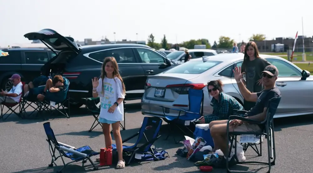 Family by their car, waving to camera from their allocated space at Skydrive, London Airshow.