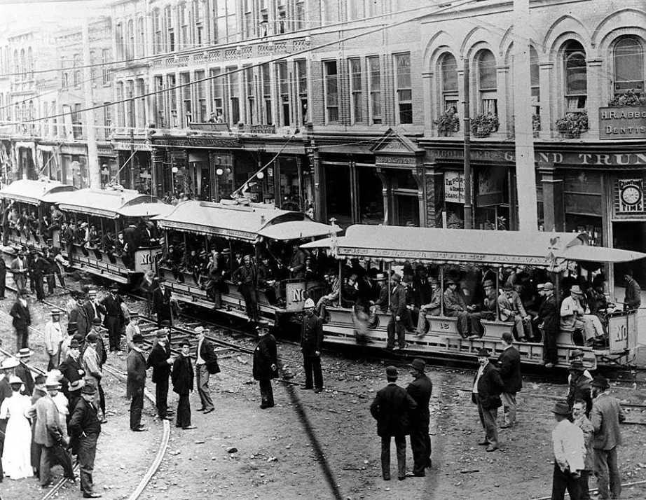 Inauguration of electric streetcar service, 1895 in London, showing crowds of people on four trolley cars. 
