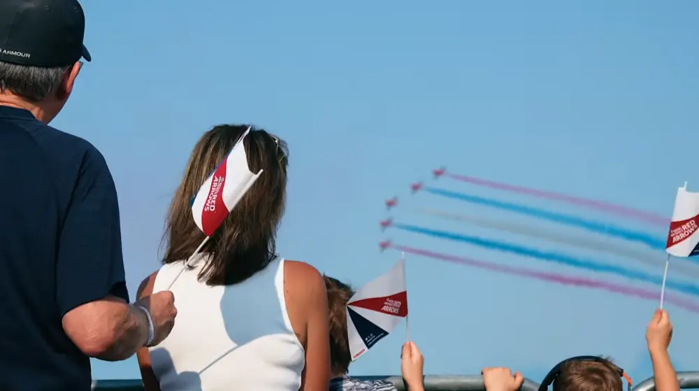 The UK's Royal Air Force Red Arrows fly by a crowd, trailing red, white, and blue smoke.
