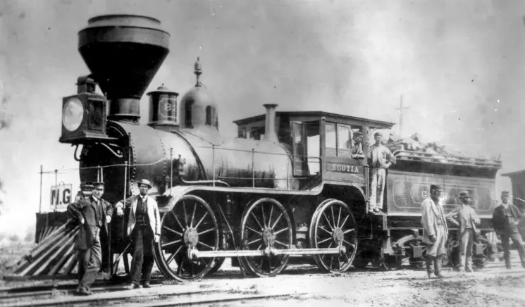 Crew standing in front of an 1860s wood fired locomotive with tender.