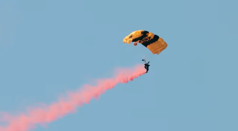 The US Army Golden Knights put on parachute displays with orange smoke trailing behind the skydiver.