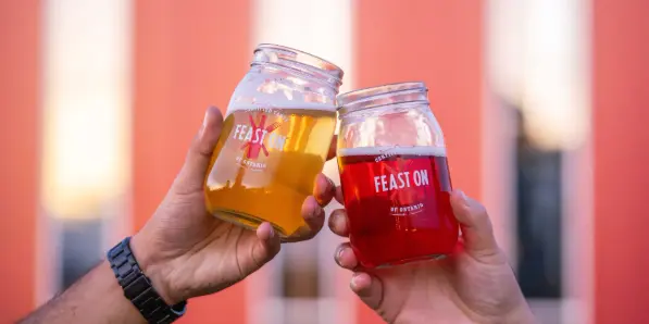 Two hands are visible, making a toast using FeastON jars.