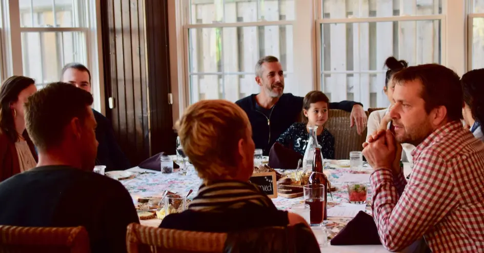 A large group of people in conversation, gathered around a large table at a restaurant enjoying their meal.