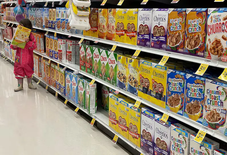 A small child in the cereal aisle of a grocery store holding a cereal box.