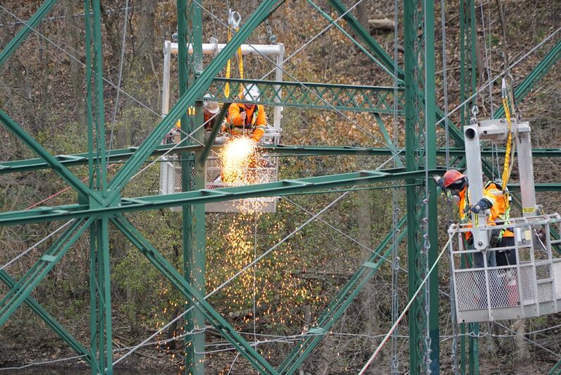 Sparks fly as workers, suspended by cranes, cut through the historic bridge to split the structure in half.